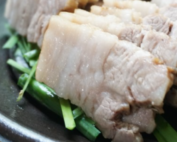 Korean boiled pork on a bed of chives on a black plate