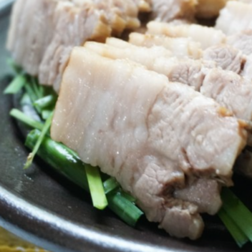 Korean boiled pork on a bed of chives on a black plate