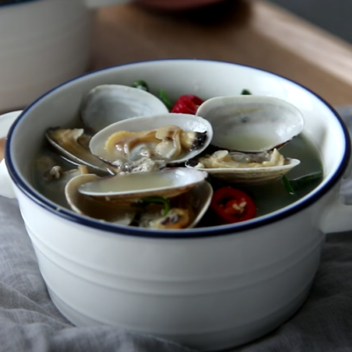 spinach clam soup in a white bowl with blue lining with handles